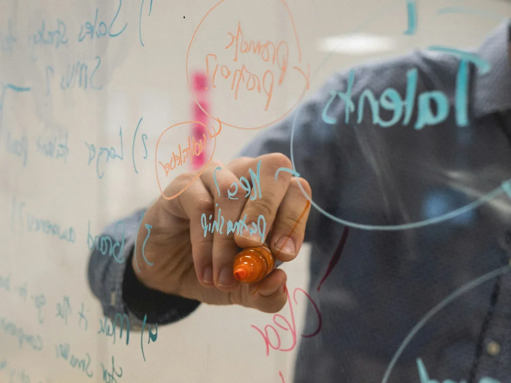 Person writing ideas on a glass whiteboard with colorful markers